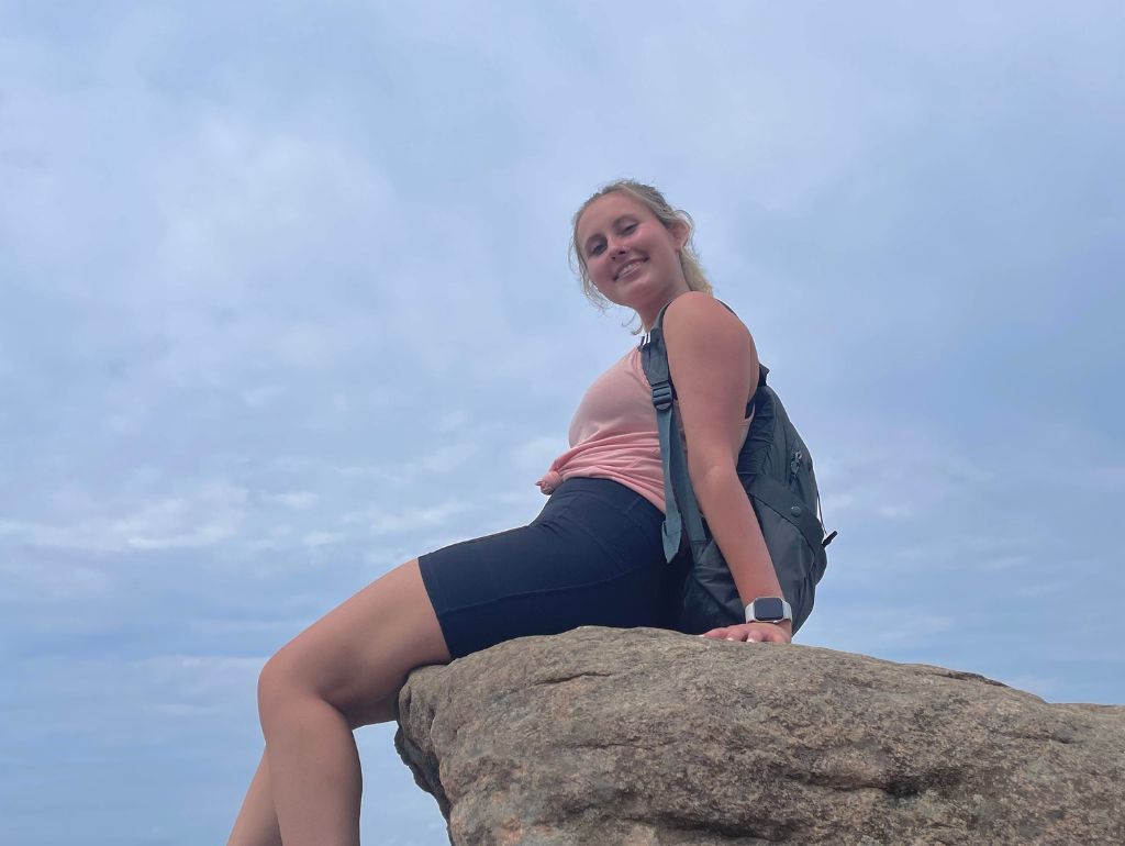 Image of Cassidy M. sitting in on a boulder.
