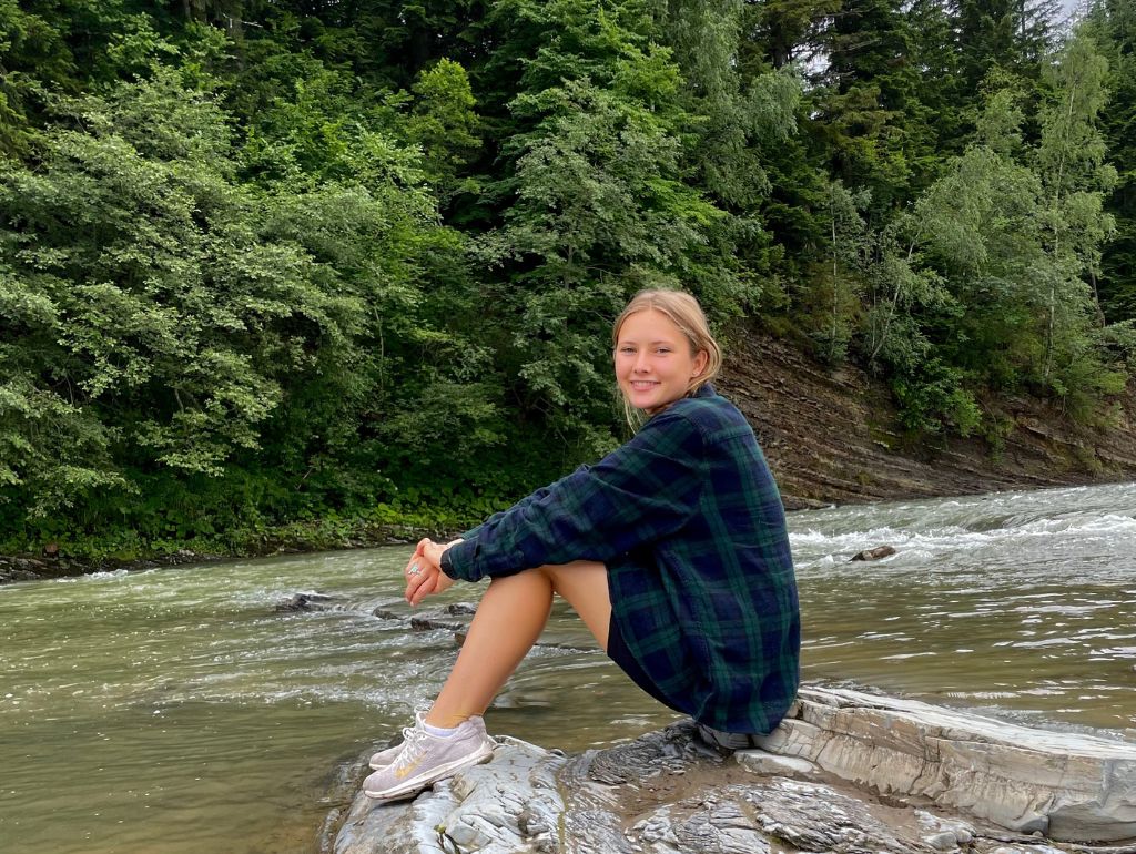 Image of Maryana S. sitting along a river bank.