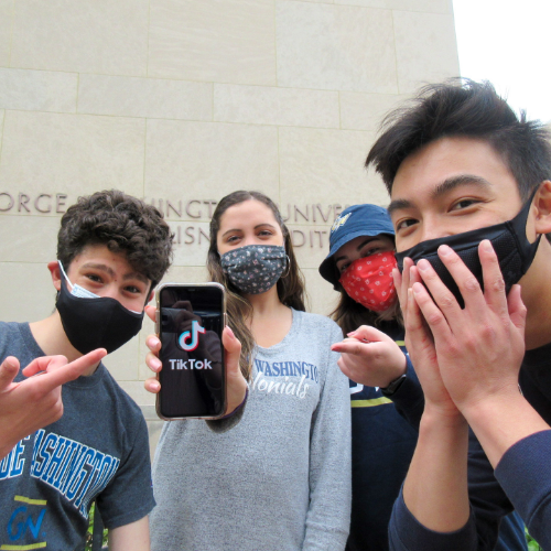 Four GW Students with masks looking excited about TikTok on a cell phone